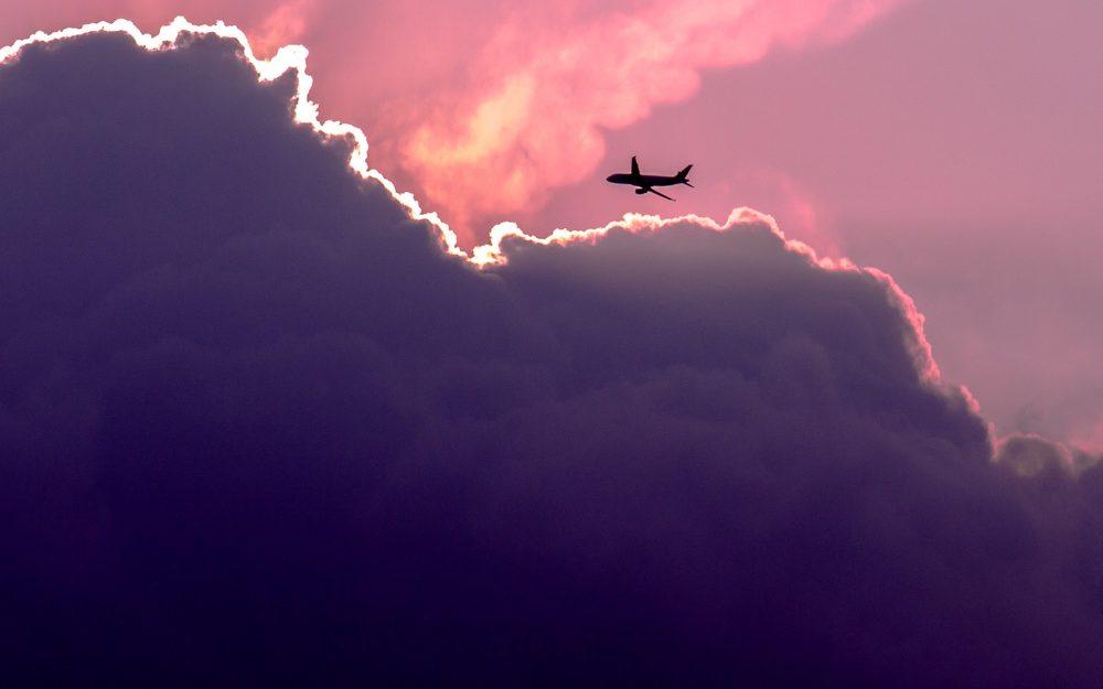 purple sky with large clouds and a plane flying