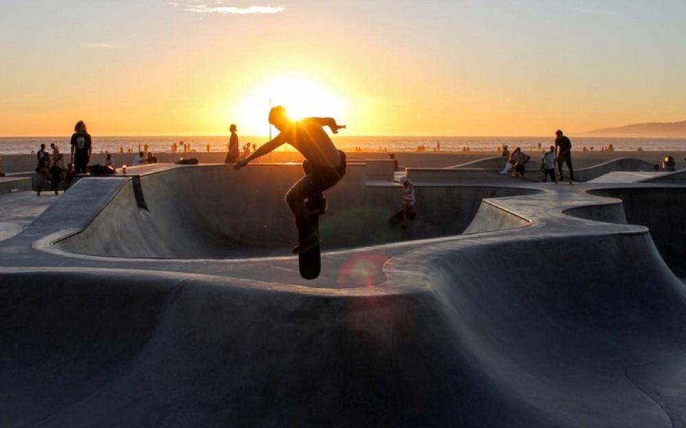Skateboarder skating at a skate park by the beach while the sun sets