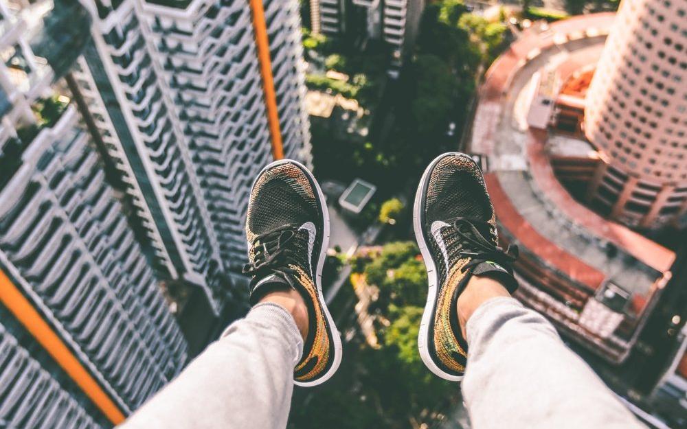person sitting on a ledge with their feet hanging over a major city 