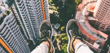 person sitting on a ledge with their feet hanging over a major city